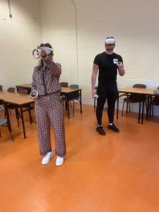 Two students standing in a classroom. Each one is wearing a Quest 2 VR headset.
